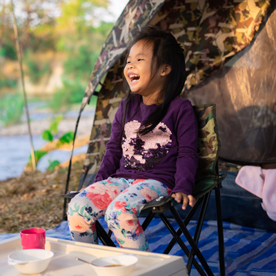 little girl sitting on the chair while going camping.The concept of outdoor activities and adventures in nature.